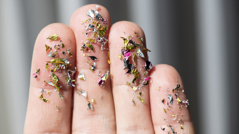 Close-up of microplastic particles in different colours sticking to a person's fingers
