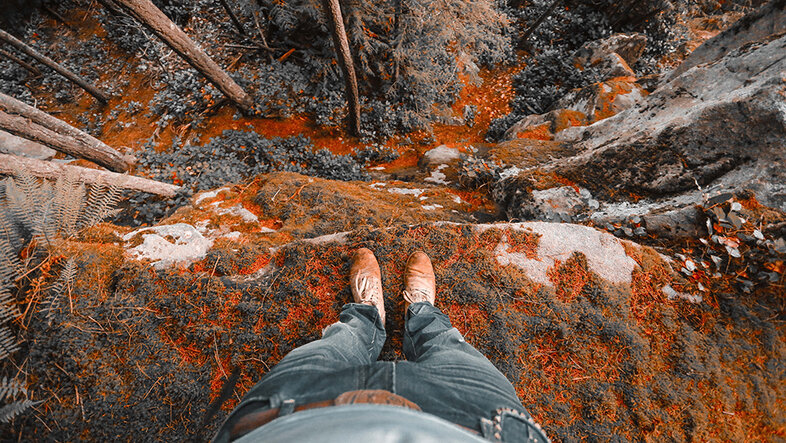 Photo taken from the first-person perspective: The legs of a hiker in front of a chasm in the forest.