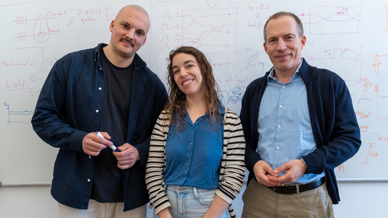 Simon Steiner, Iris Agresti und Philip Walther vor dem mit Formeln beschriebenen Whiteboard