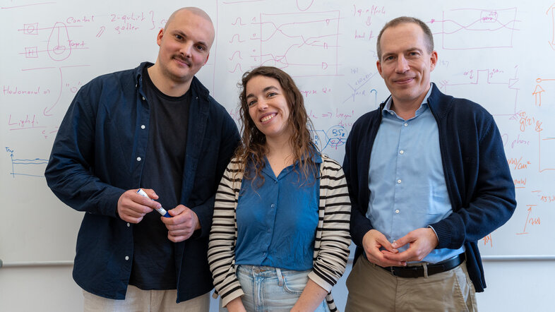 Simon Steiner, Iris Agresti und Philip Walther vor dem mit Formeln beschriebenen Whiteboard