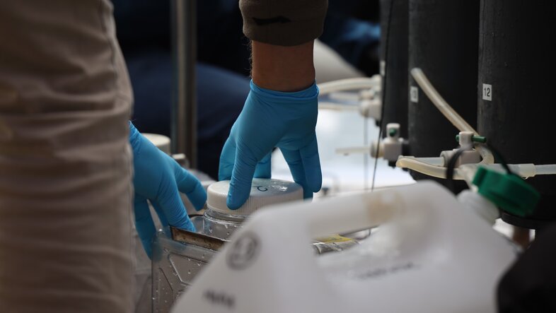 Gloved hands handle lab containers and tubes, suggesting sample collection or experiment work.