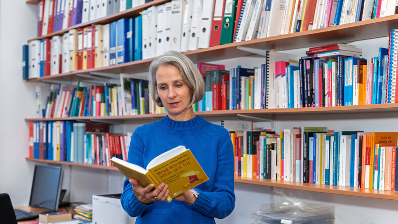 Ulrike Zartler vor einem Bücherregal mit einem Buch in der Hand