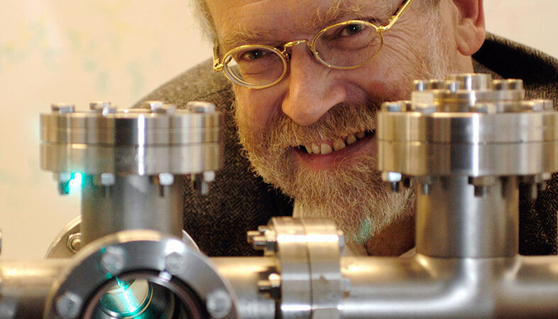 Portrait photo of Anton Zeilinger in the laboratory looking out from behind a piece of research equipment