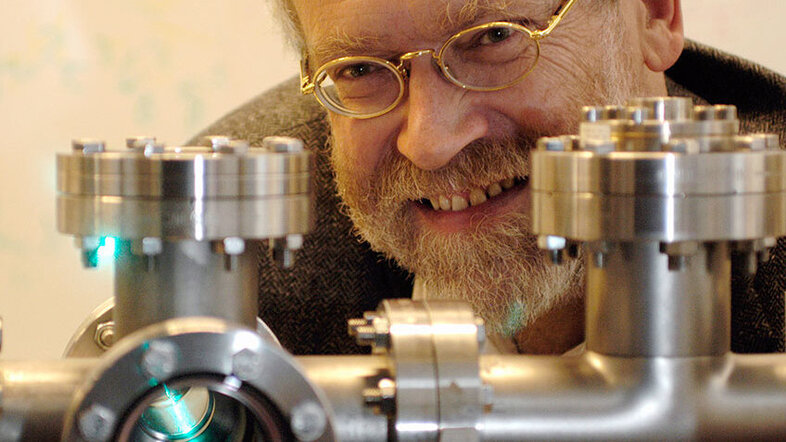 Porträtfoto von Anton Zeilinger im Labor schaut hinter einem Forschungsgerät hervor