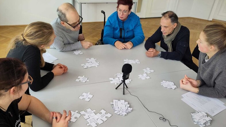 Gruppe sitzt am Tisch mit Puzzleteilen