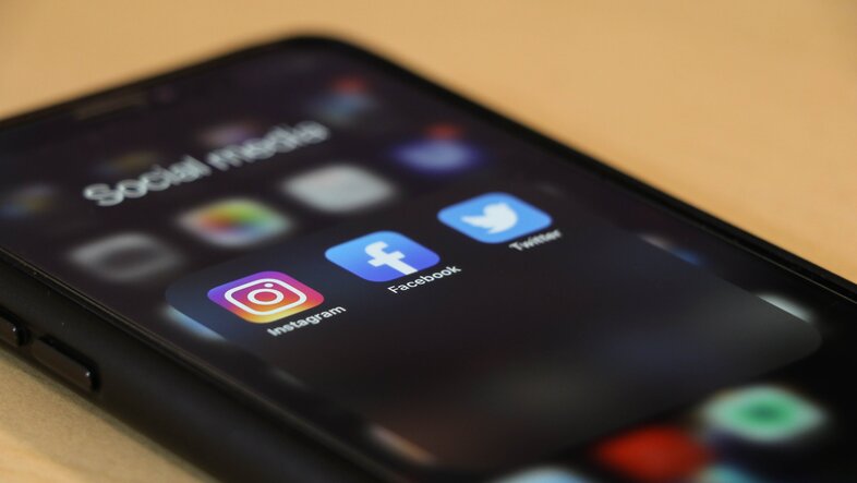 On the screen of a mobile phone, you can see the icons of Instagram, Facebook and Twitter.