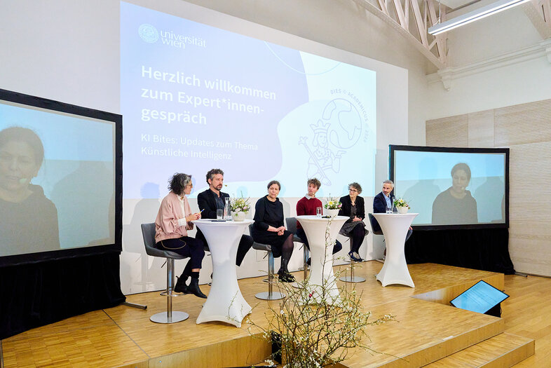 Podiumsdiskussion am Dies Academicus an der Uni Wien mit dem Titel KI Bites. Iris Eisenberger sitzt mit 5 wieteren Personen am Podium.