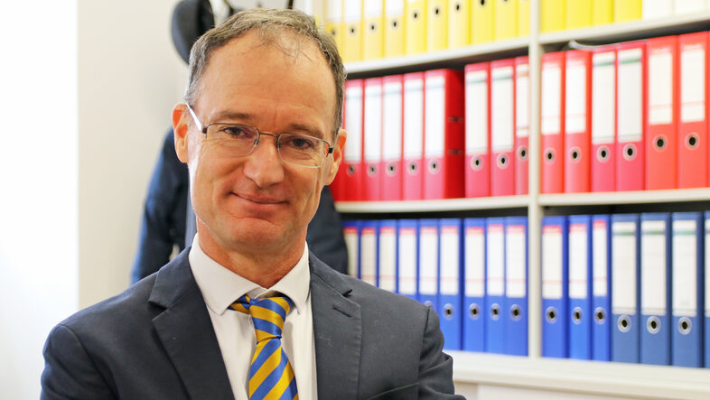 © Wolfgang Mueller in seinem Büro. Er trägt eine blau-gelb-gestreifte Krawatte.