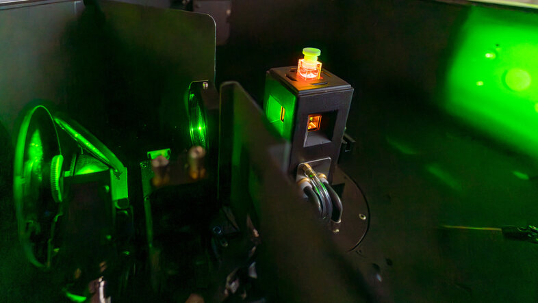 A sample containing a red liquid in a sample holder is being hit a green laser light