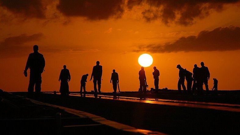 © Die Silhouetten von 13 Personen bei der Bauarbeit mit flach stehender Sonne im Hintergrund