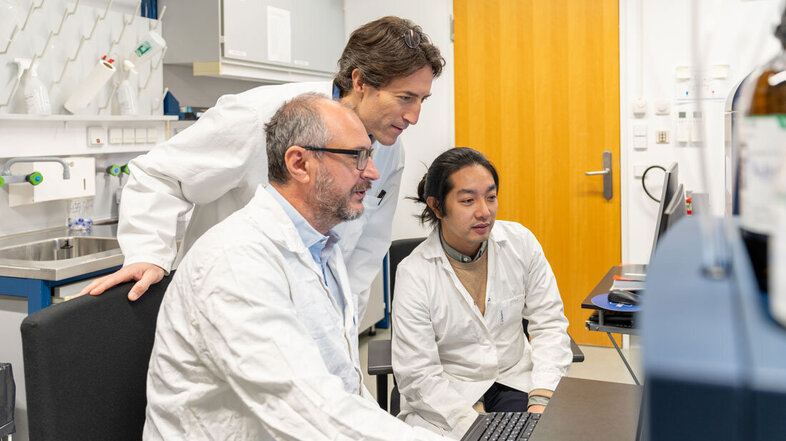 Three researchers in front of a screen discussing data from the mass spectrometer