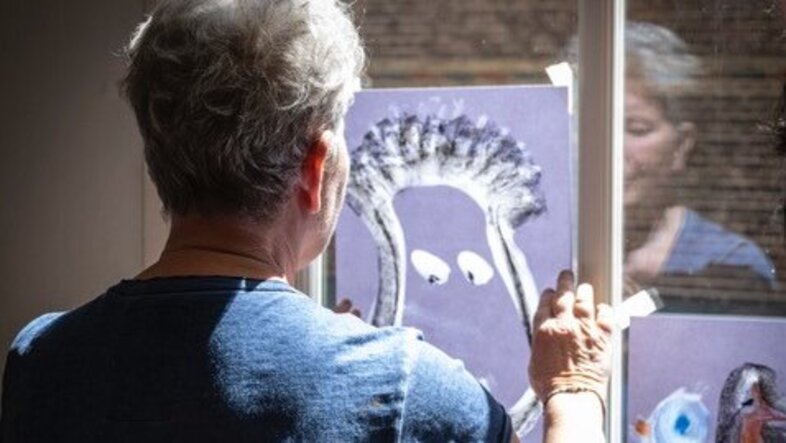 Ältere Frau vor einem Fenster mit gemalten Bildern