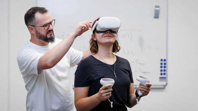 Robert Böhm hilft Kollegin Sabrina Forst, eine Virtual Reality-Brille aufzusetzen
