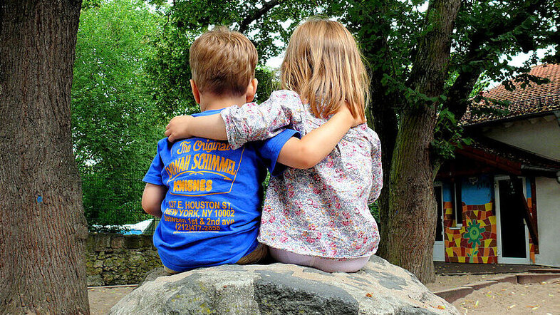 Zwei Kinder umarmen sich sitzend auf einem Stein