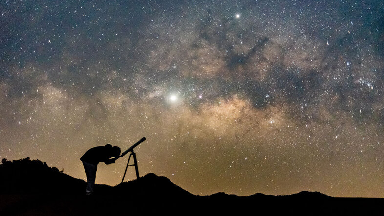 Human silhouette with a telescope under a night sky with the Milky Way