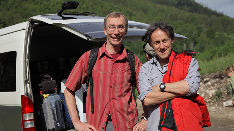 Two men in hiking clothes in front of the open booth of a caravan.