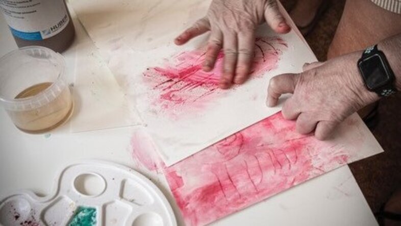Hände einer Person verteilen Farbe auf einem Blatt Papier