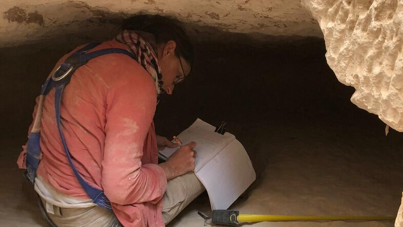Delphine Driaux inspects a burial chamber at the bottom of a rock cut tomb