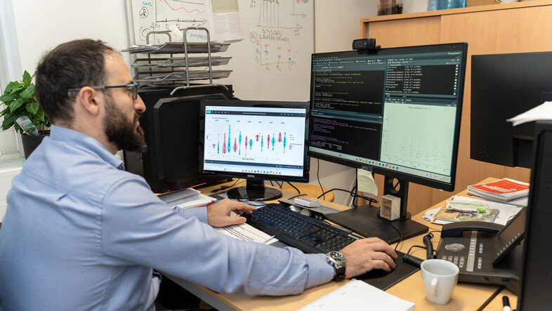Forscher sitzt an zwei Bildschirmen und wertet Daten aus
