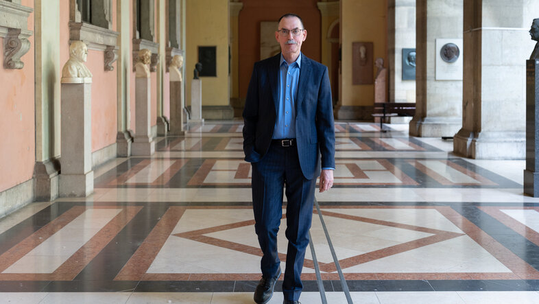A man in a suit walks straight on towards the viewer in a hallway