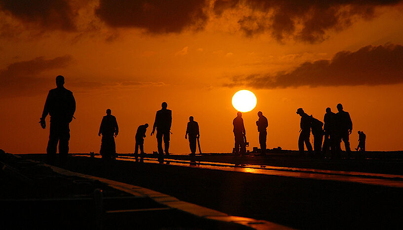 Die Silhouetten von 13 Personen bei der Bauarbeit mit flach stehender Sonne im Hintergrund